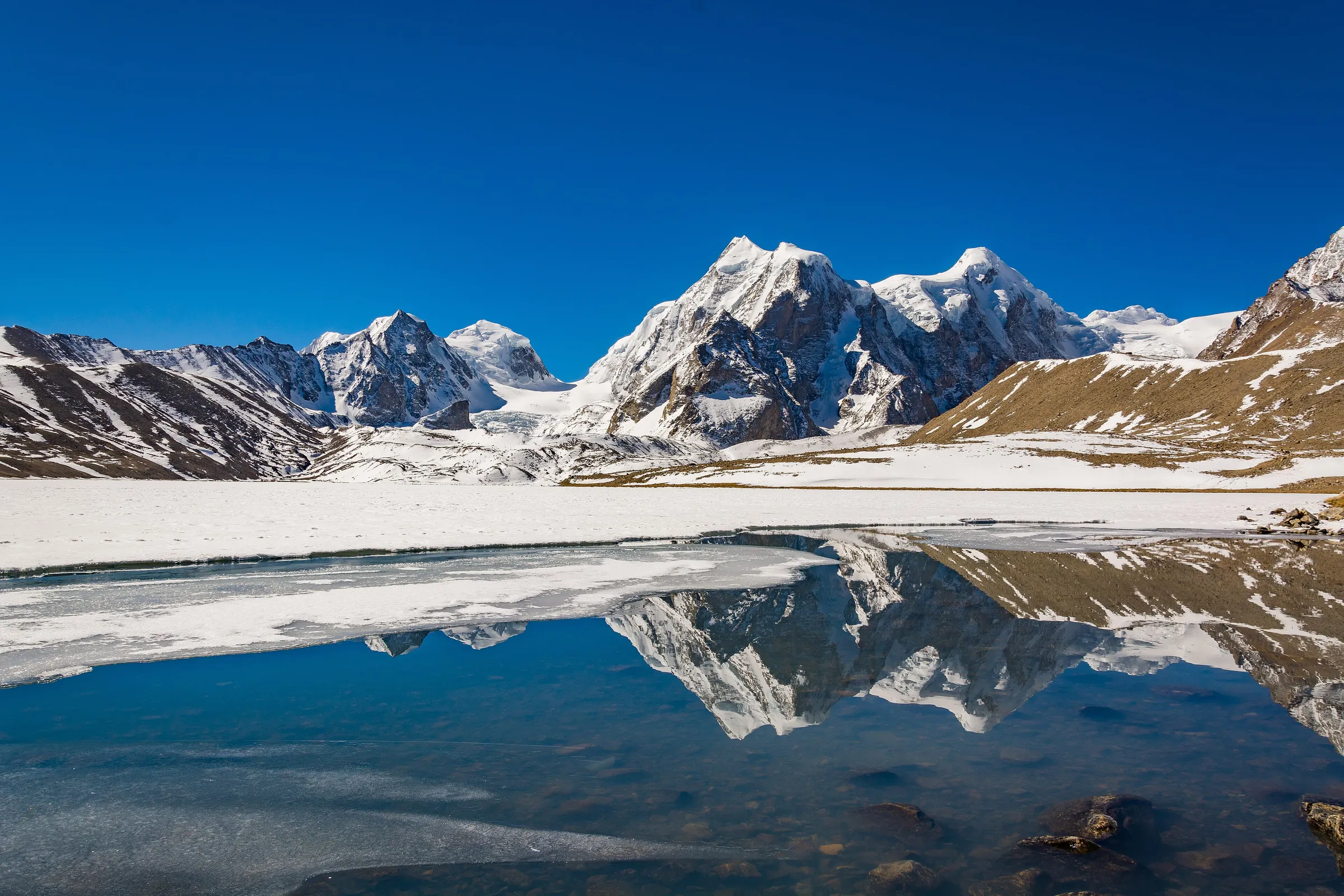 Snow peaks reflected in a partly frozen Gurudongmar Lake, North Sikkim